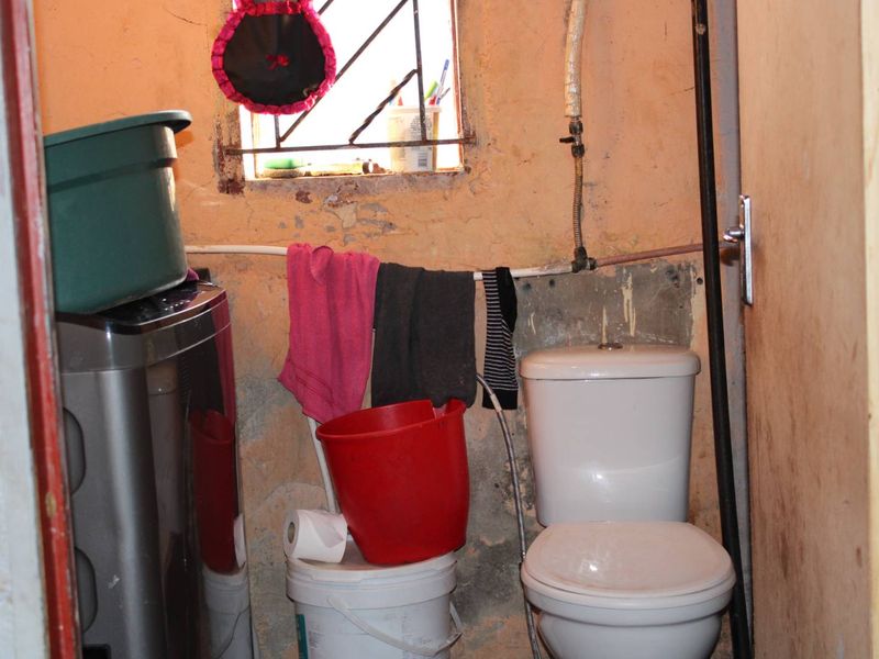 A small bathroom featuring a toilet and exposed plumbing, requiring significant maintenance and cosmetic updates to the wall finishes.
