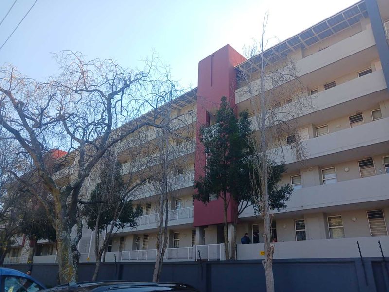 Exterior view of a multi-story apartment building featuring balconies and secure perimeter wall with electric fencing.