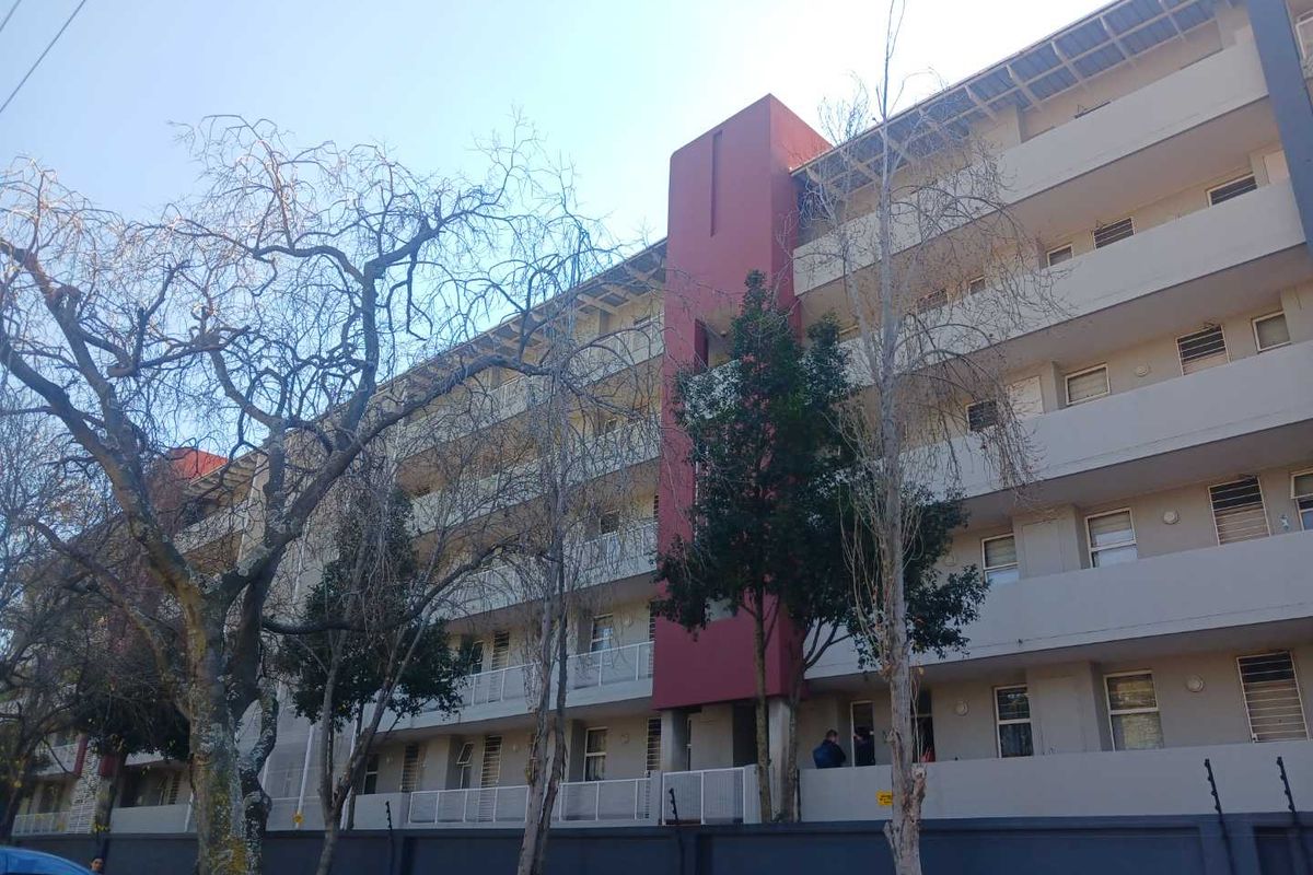 Exterior view of a multi-story apartment building featuring balconies and secure perimeter wall with electric fencing.