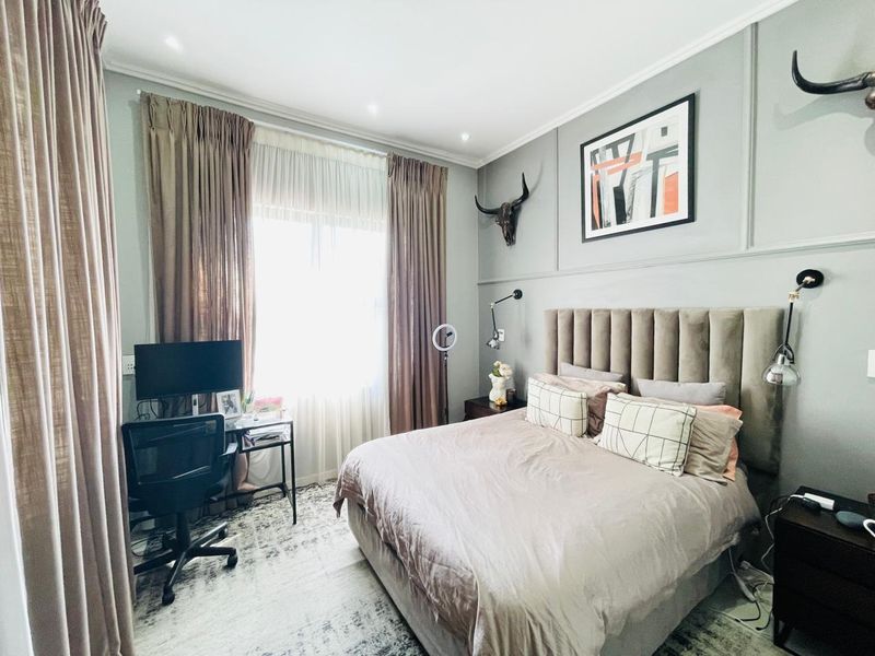 A well-maintained bedroom featuring decorative wall paneling, recessed downlighting, and large windows with full-length curtains.