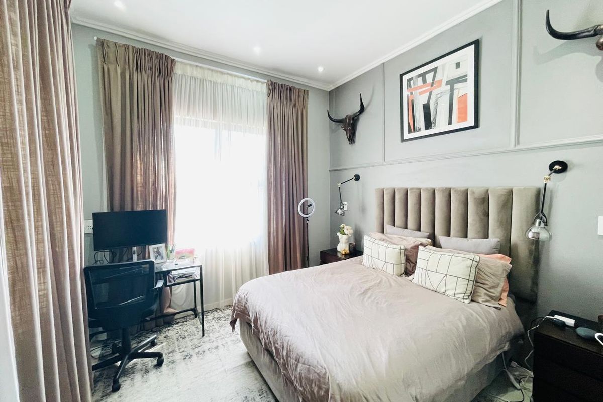 A well-maintained bedroom featuring decorative wall paneling, recessed downlighting, and large windows with full-length curtains.