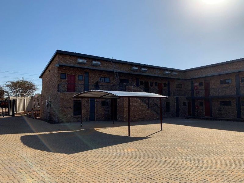 Exterior view of a face brick apartment complex featuring a paved courtyard, covered carport, and external metal staircases providing access to upper levels.