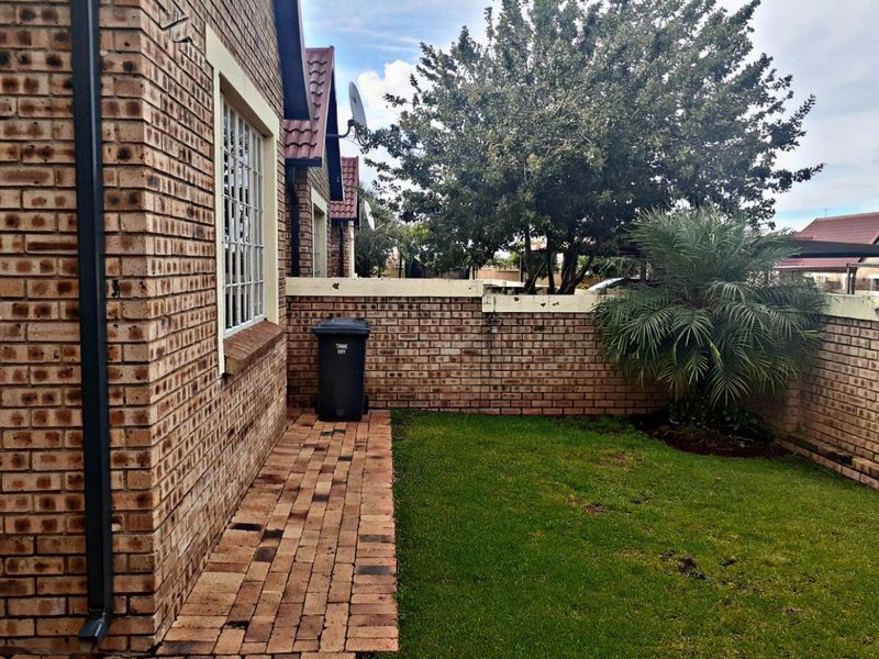 A private rear garden area featuring a paved walkway, established lawn, and face brick boundary walls.