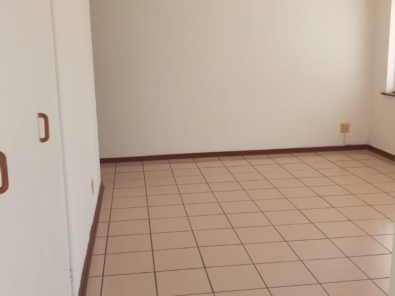 An empty bedroom featuring neutral tiled flooring and built-in cupboards, providing a clean and versatile space ready for personalization.
