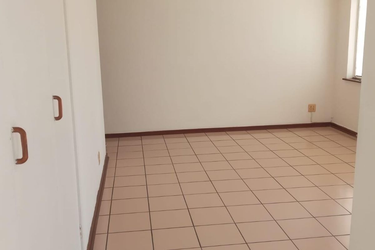 An empty bedroom featuring neutral tiled flooring and built-in cupboards, providing a clean and versatile space ready for personalization.
