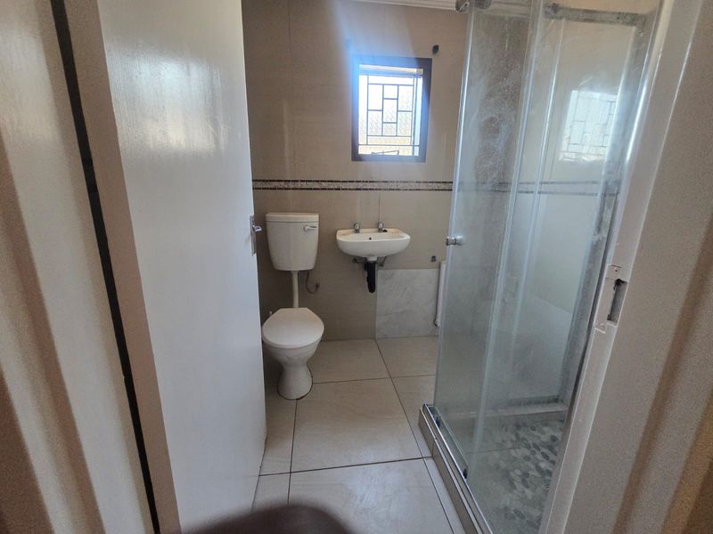 A functional bathroom featuring a shower enclosure, wall-mounted basin, and toilet, finished with neutral wall and floor tiles.