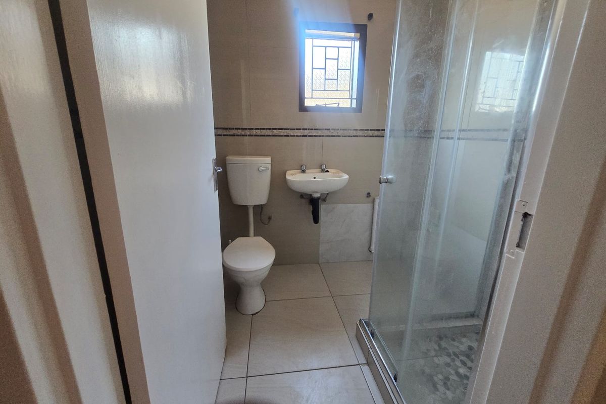 A functional bathroom featuring a shower enclosure, wall-mounted basin, and toilet, finished with neutral wall and floor tiles.