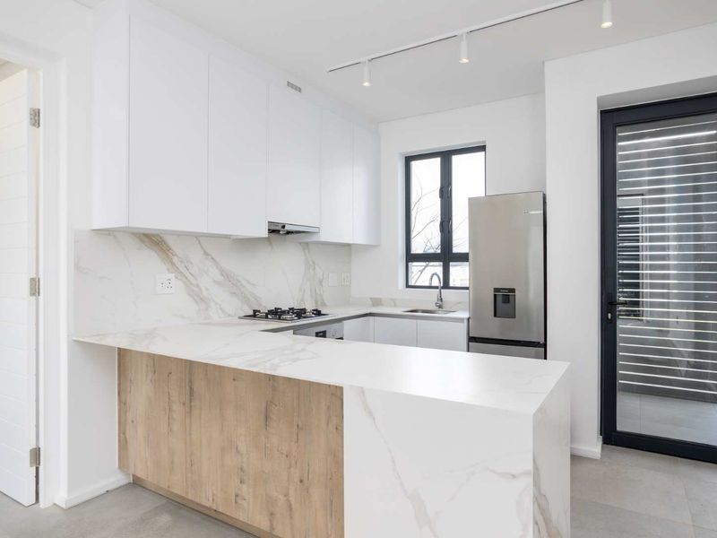 Modern kitchen featuring white cabinetry, marble-look stone countertops, gas hob, extractor fan, and sleek track lighting, offering a clean and contemporary aesthetic.