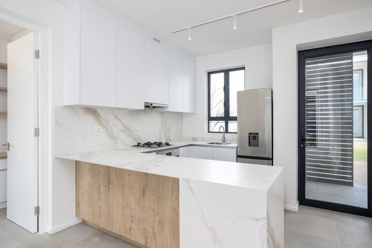 Modern kitchen featuring white cabinetry, marble-look stone countertops, gas hob, extractor fan, and sleek track lighting, offering a clean and contemporary aesthetic.