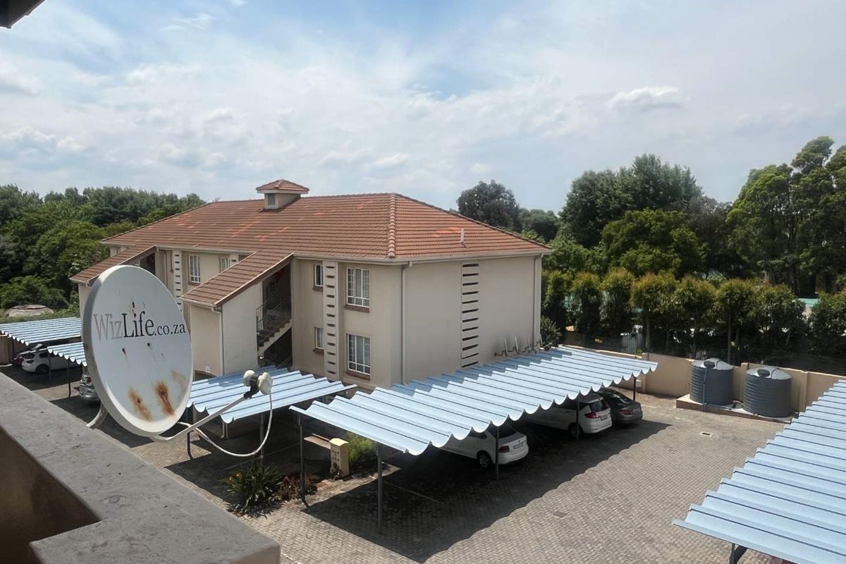 Exterior view of the apartment complex featuring a paved parking area with covered carports and water storage tanks.