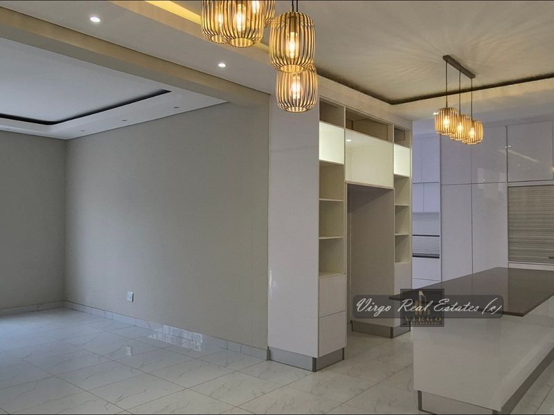 Modern open-plan living and kitchen area featuring high-gloss cabinetry, a central island, recessed lighting, and polished tiled flooring throughout.