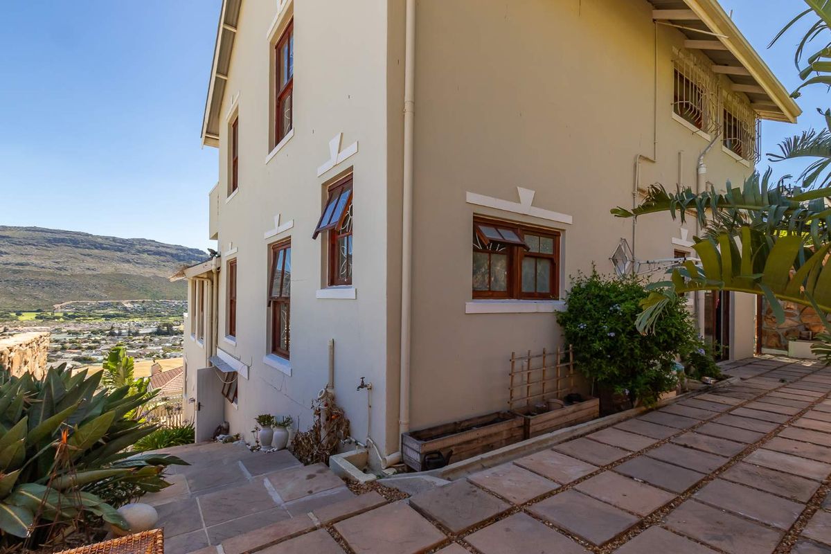 Side elevation of the house featuring paved pathways, established garden beds, and timber-framed windows with a scenic mountain and valley view.