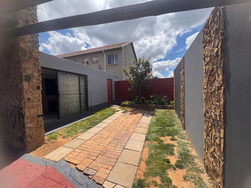 A private rear courtyard featuring a paved walkway, stone-clad feature walls, and a covered patio area with sliding glass doors.