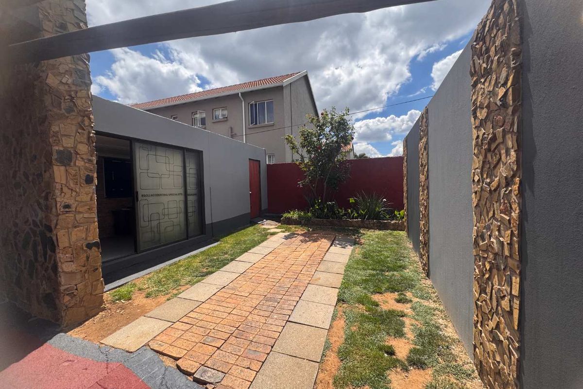 A private rear courtyard featuring a paved walkway, stone-clad feature walls, and a covered patio area with sliding glass doors.