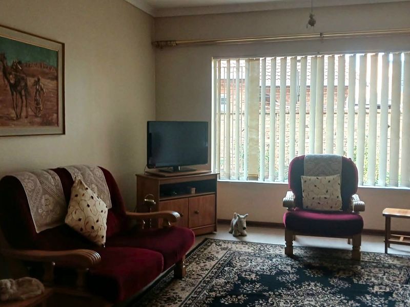 A comfortable living room featuring large windows with vertical blinds, providing natural light and a neutral wall finish.