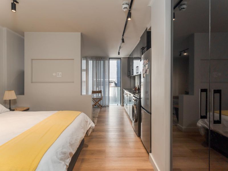 Modern open-plan studio apartment featuring a compact kitchen with built-in cabinetry, integrated laundry, track lighting, and sleek laminate flooring.
