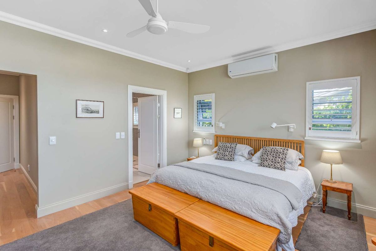 A well-maintained bedroom featuring timber flooring, a ceiling fan, split-system air conditioning, and plantation shutters.