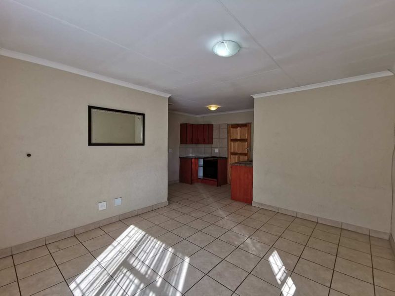 An open-plan living and kitchen area featuring tiled flooring, built-in cabinetry, and an integrated oven, offering a functional blank canvas for interior design.