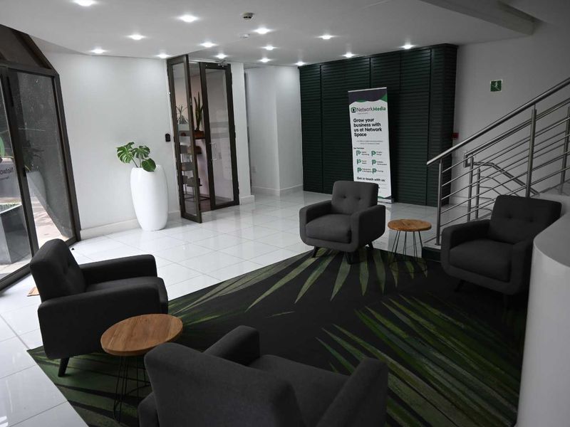 Modern office building entrance lobby featuring tiled flooring, recessed ceiling lights, a staircase with metal railings, and decorative wall paneling.