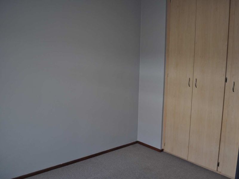 A clean, empty bedroom featuring neutral grey walls, carpeted flooring, and built-in wooden cupboards.