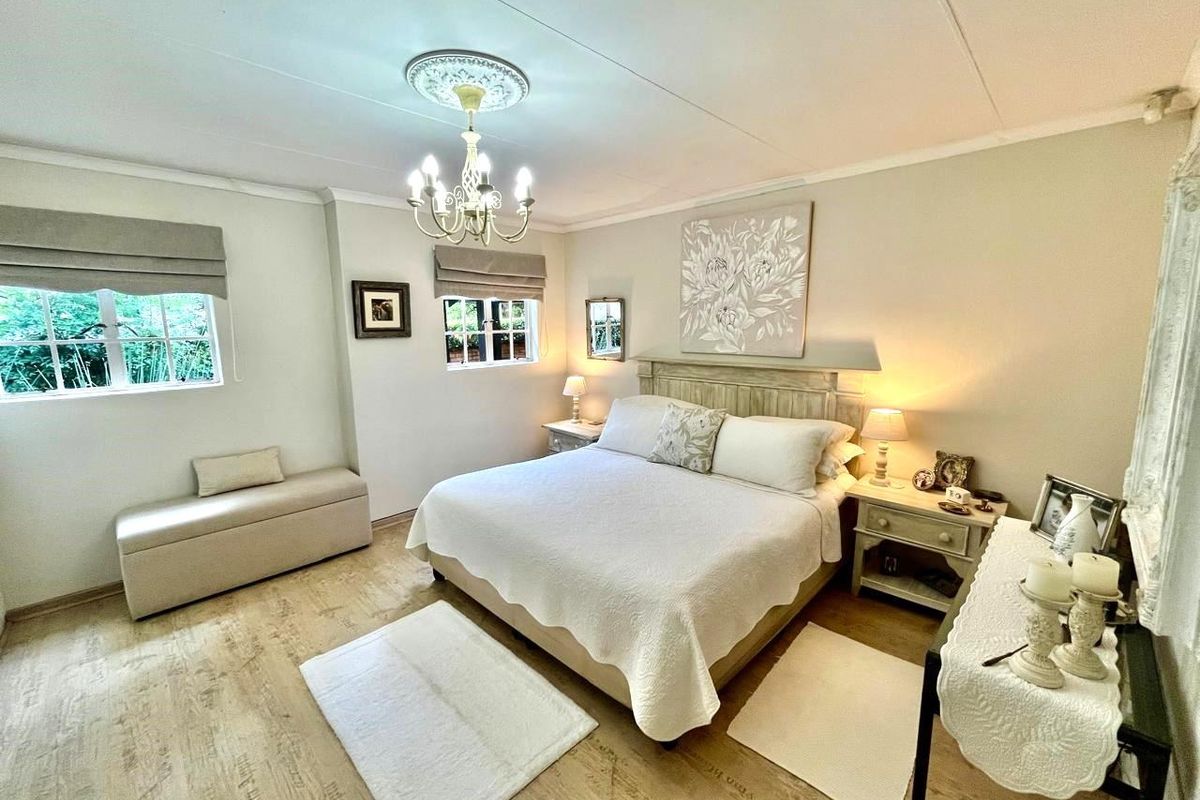 A well-maintained bedroom featuring wood-look flooring, decorative ceiling rose with chandelier, and built-in window treatments.