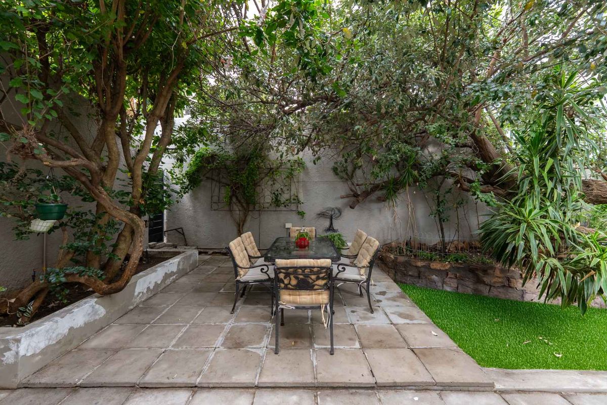 A private rear garden area featuring paved patio space, established trees, and a small artificial lawn section, ideal for outdoor dining.