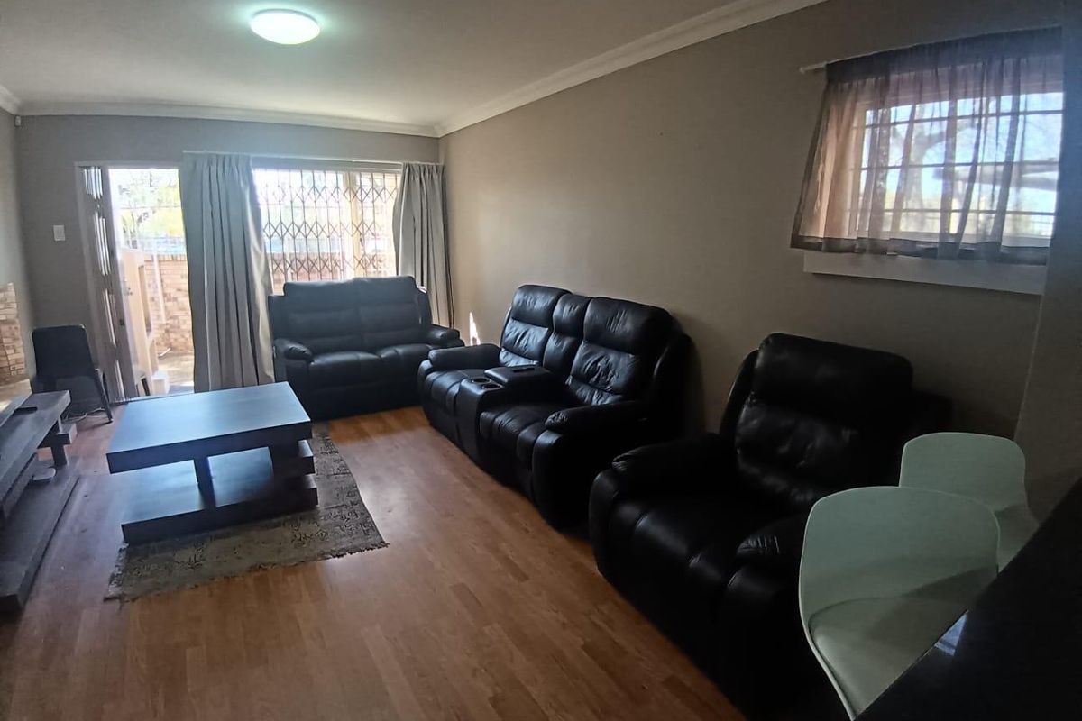 A spacious living room featuring laminate flooring, a sliding door with security gate, and neutral wall finishes, offering a comfortable and functional living space.