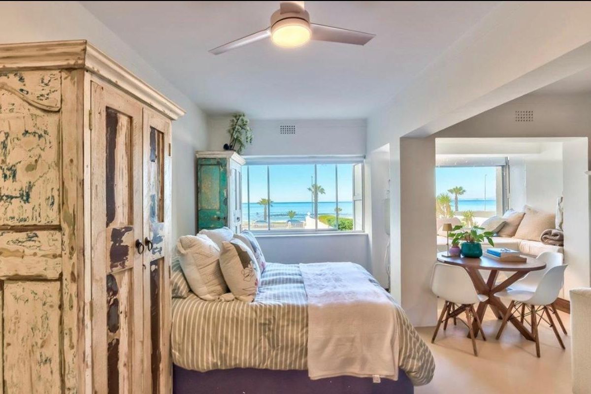 A bright bedroom featuring a ceiling fan and large windows with direct ocean views, creating a serene and airy coastal living space.