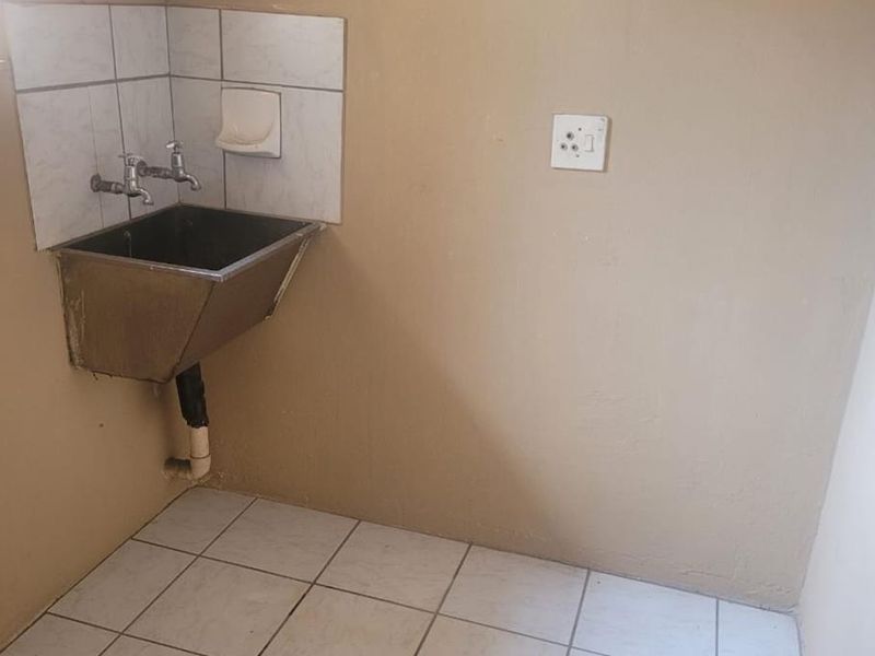 A functional laundry area featuring a stainless steel utility sink, tiled splashback, and tiled flooring, providing a practical space for household utility tasks.
