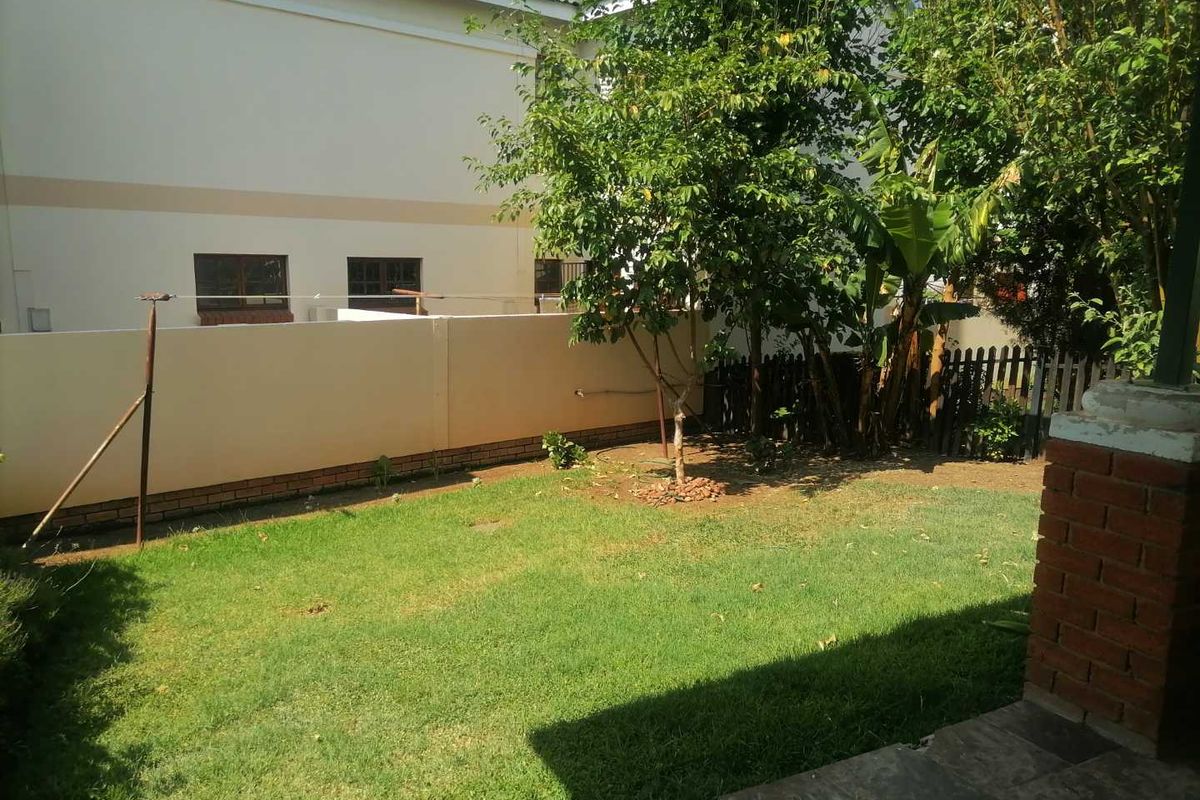 A private rear garden area featuring a lawn, established trees, and a perimeter boundary wall.