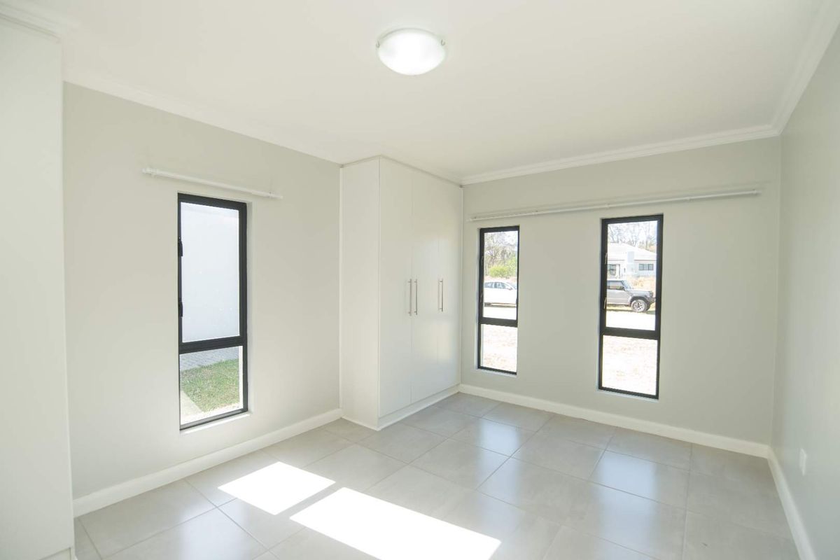 A bright, modern bedroom featuring neutral tiled flooring, built-in cabinetry, and large windows with dark frames providing ample natural light.