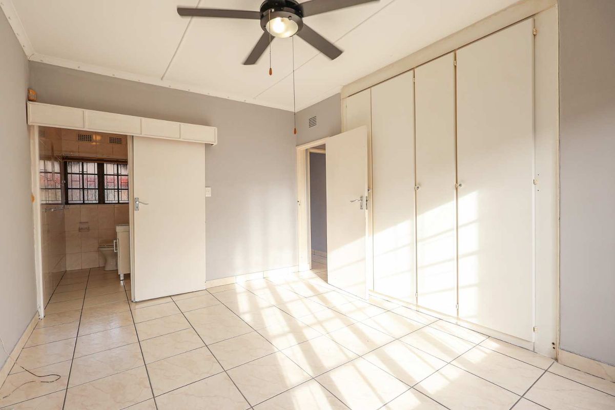 A bedroom featuring built-in wardrobes, tiled flooring, a ceiling fan, and an adjoining en-suite bathroom.