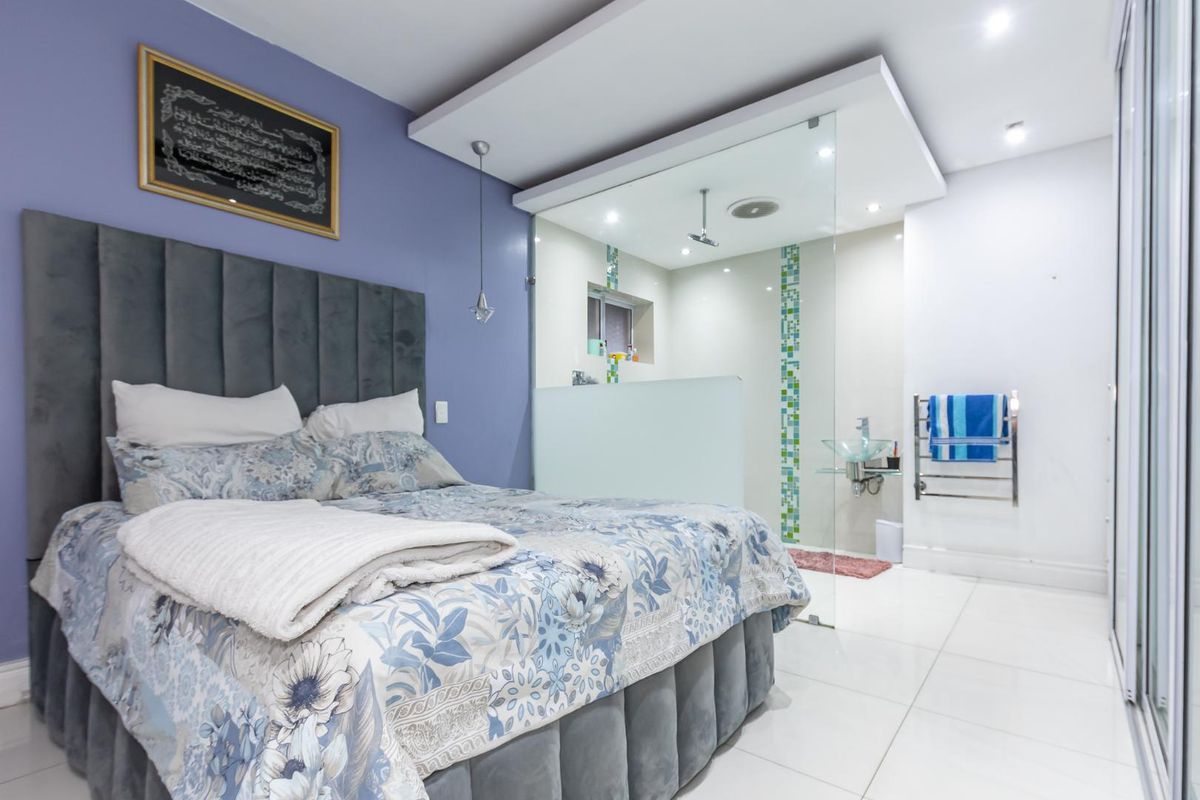 Modern bedroom featuring an open-plan en-suite bathroom with a glass-enclosed shower, contemporary vessel sink, and sleek tiled flooring.