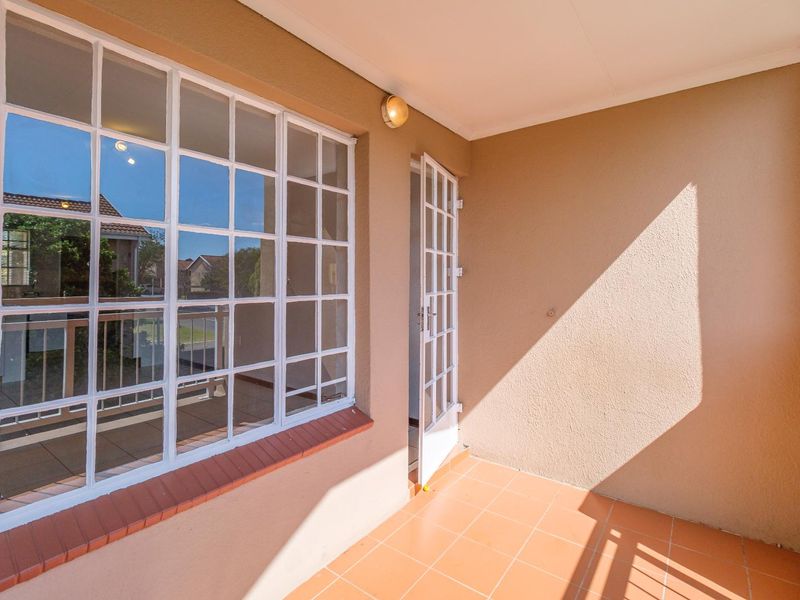 A clean, covered balcony featuring tiled flooring, a classic grid window, and a white french door leading into the apartment.