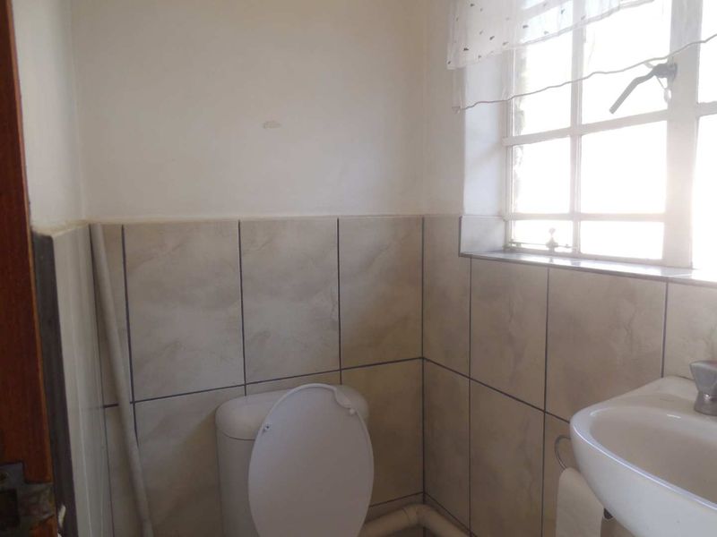 A compact bathroom featuring a pedestal basin, toilet, and tiled splashback, with visible plumbing and natural light from a window.
