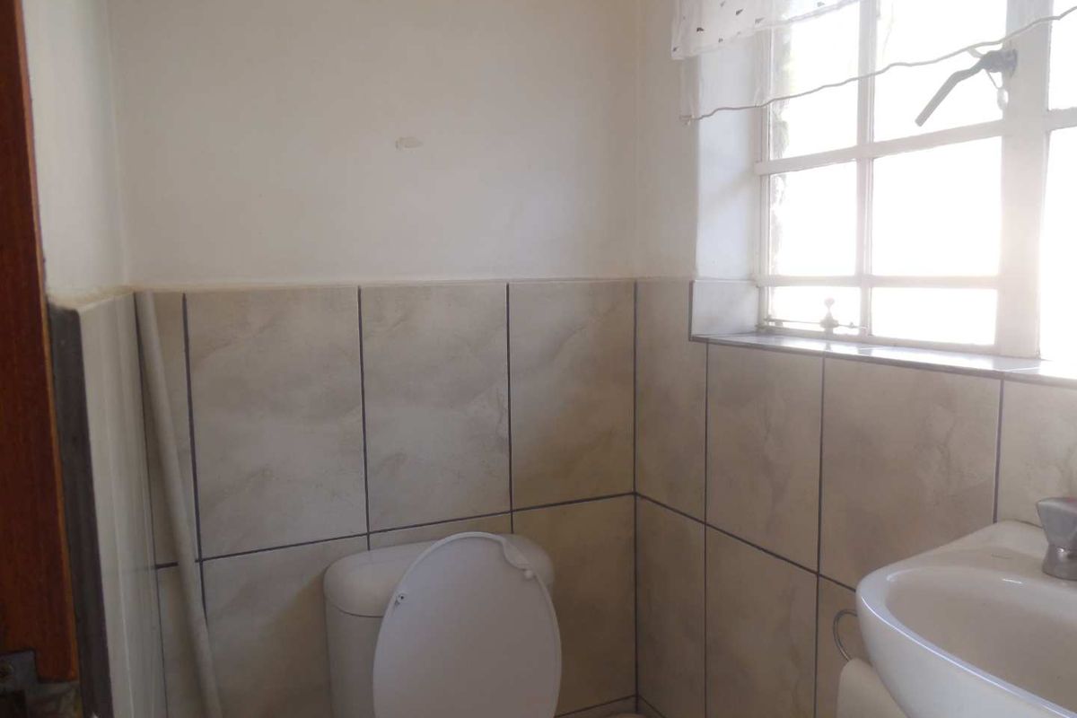 A compact bathroom featuring a pedestal basin, toilet, and tiled splashback, with visible plumbing and natural light from a window.