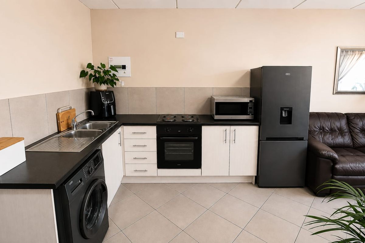 A functional kitchen area featuring light-toned cabinetry, dark countertops, a built-in oven, electric hob, and tiled flooring, providing a clean and practical workspace.