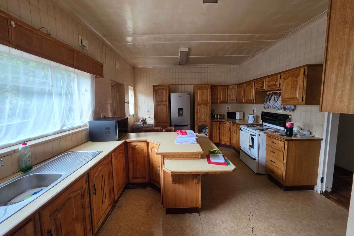 A spacious, dated kitchen featuring extensive wooden cabinetry, a central breakfast bar, and tiled wall finishes, offering significant potential for a modern renovation.