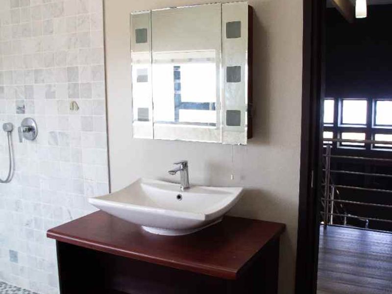 A modern bathroom featuring a vessel sink on a dark wood vanity, a tiled shower enclosure, and a mirrored medicine cabinet.