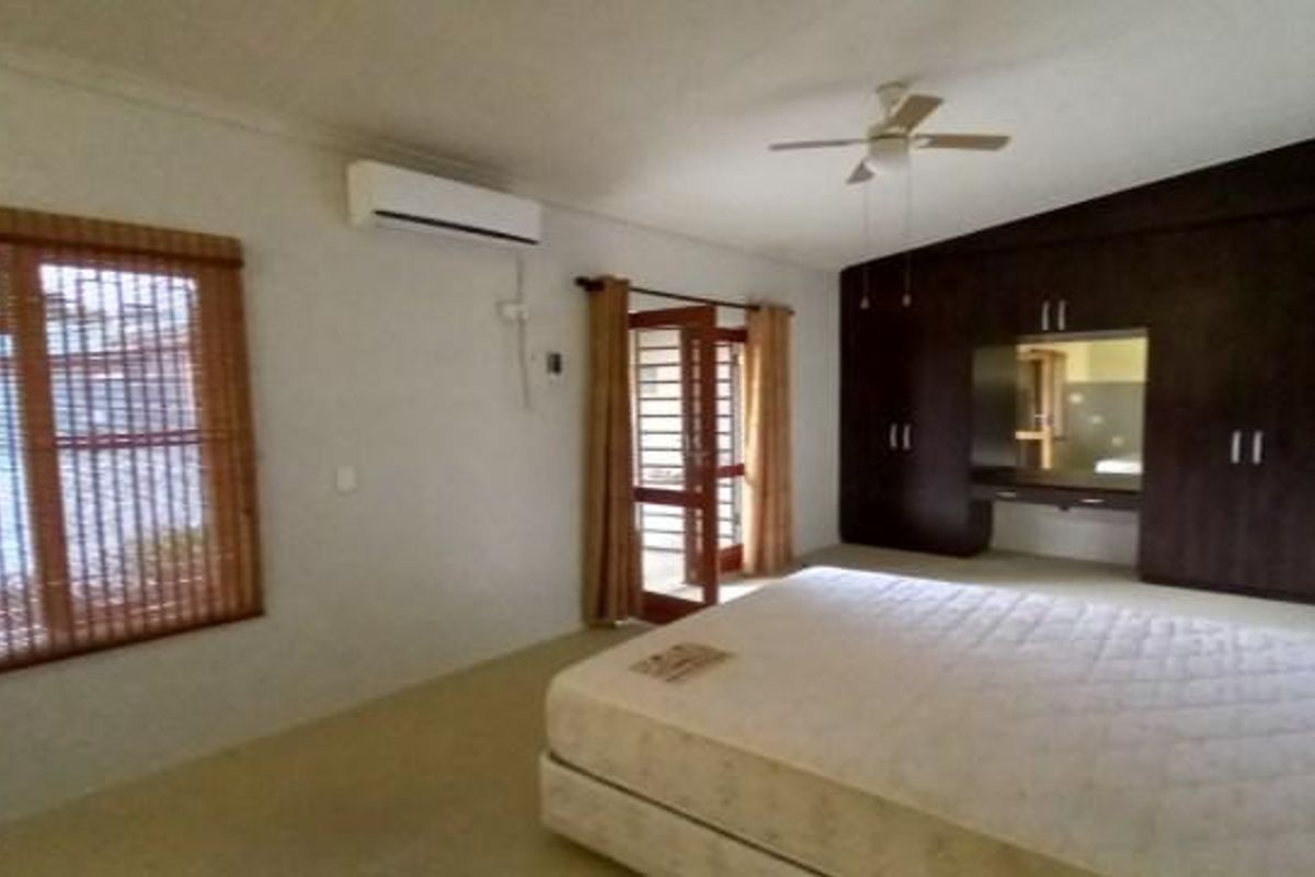 Spacious bedroom featuring built-in dark wood cabinetry, a ceiling fan, and a wall-mounted air conditioning unit with direct access to an outdoor area.