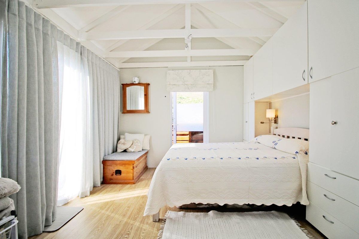 A bright bedroom featuring a vaulted ceiling with exposed beams, built-in cabinetry, and large windows with floor-to-ceiling curtains.