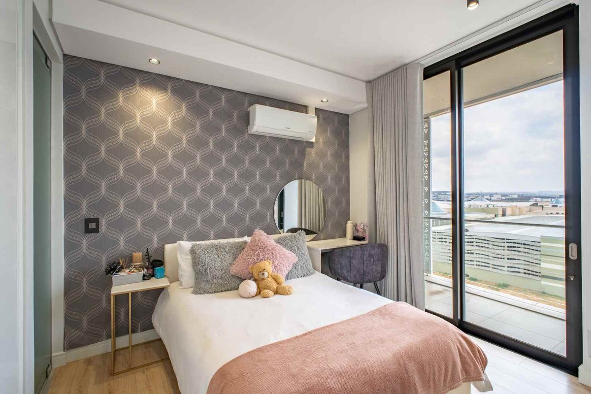 Modern bedroom featuring patterned wallpaper, split-system air conditioning, and large sliding glass doors opening onto a private balcony with expansive views.