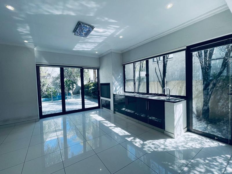 Spacious open-plan living area featuring sleek built-in cabinetry, a modern sink, tiled flooring, and large sliding glass doors opening to the outdoor pool area.