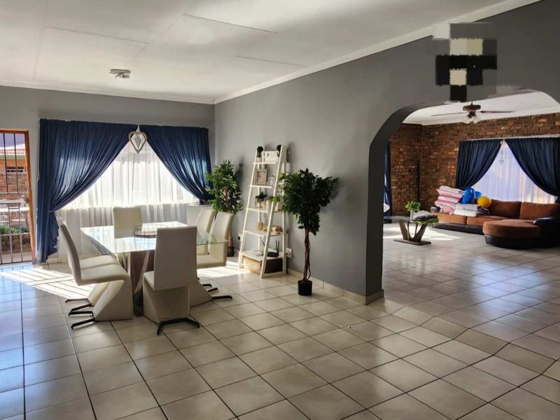 Spacious open-plan living and dining area featuring tiled flooring, an arched transition, and an exposed brick feature wall.