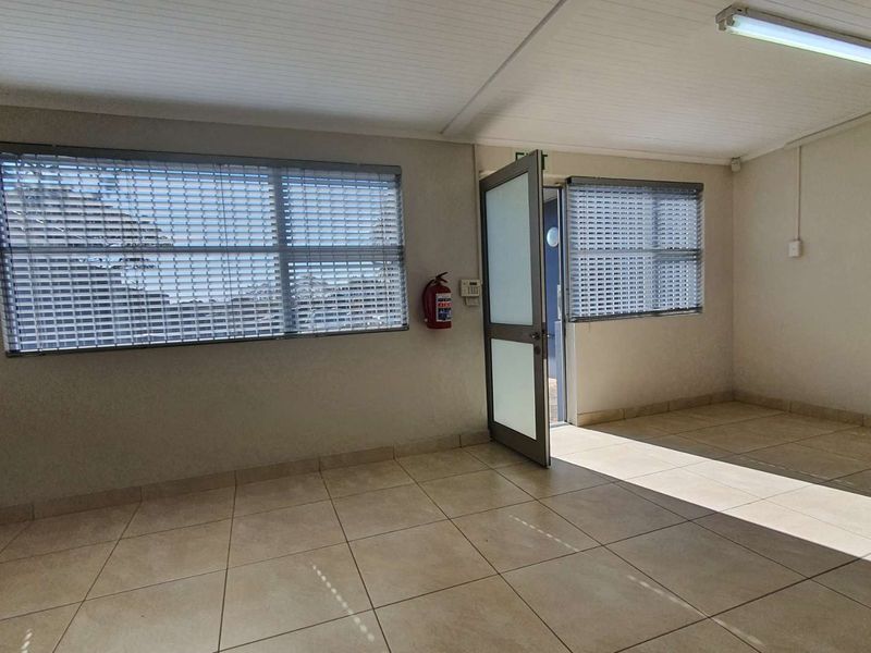 A bright, empty office space featuring tiled flooring, security shutters on windows, and a functional layout suitable for a professional workspace.