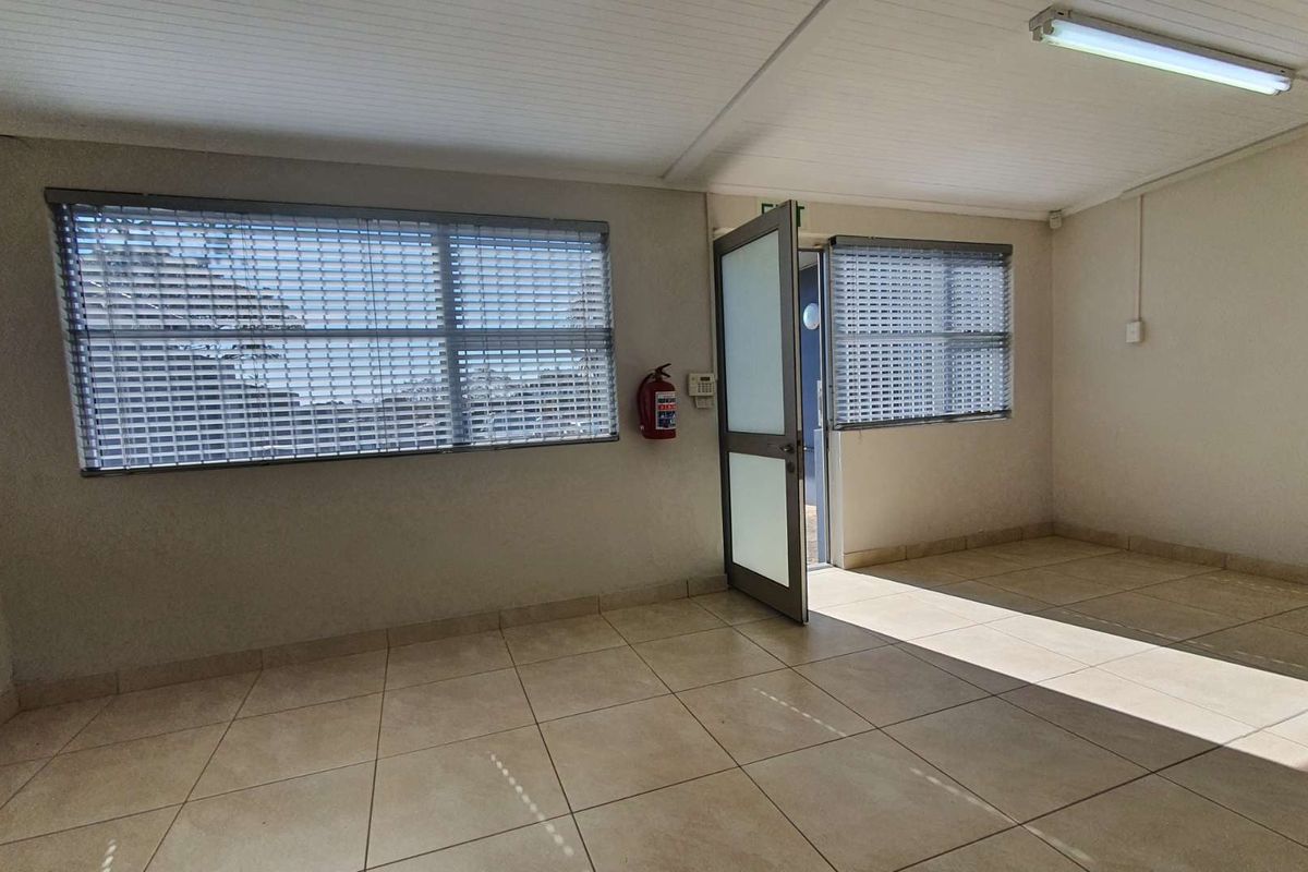 A bright, empty office space featuring tiled flooring, security shutters on windows, and a functional layout suitable for a professional workspace.