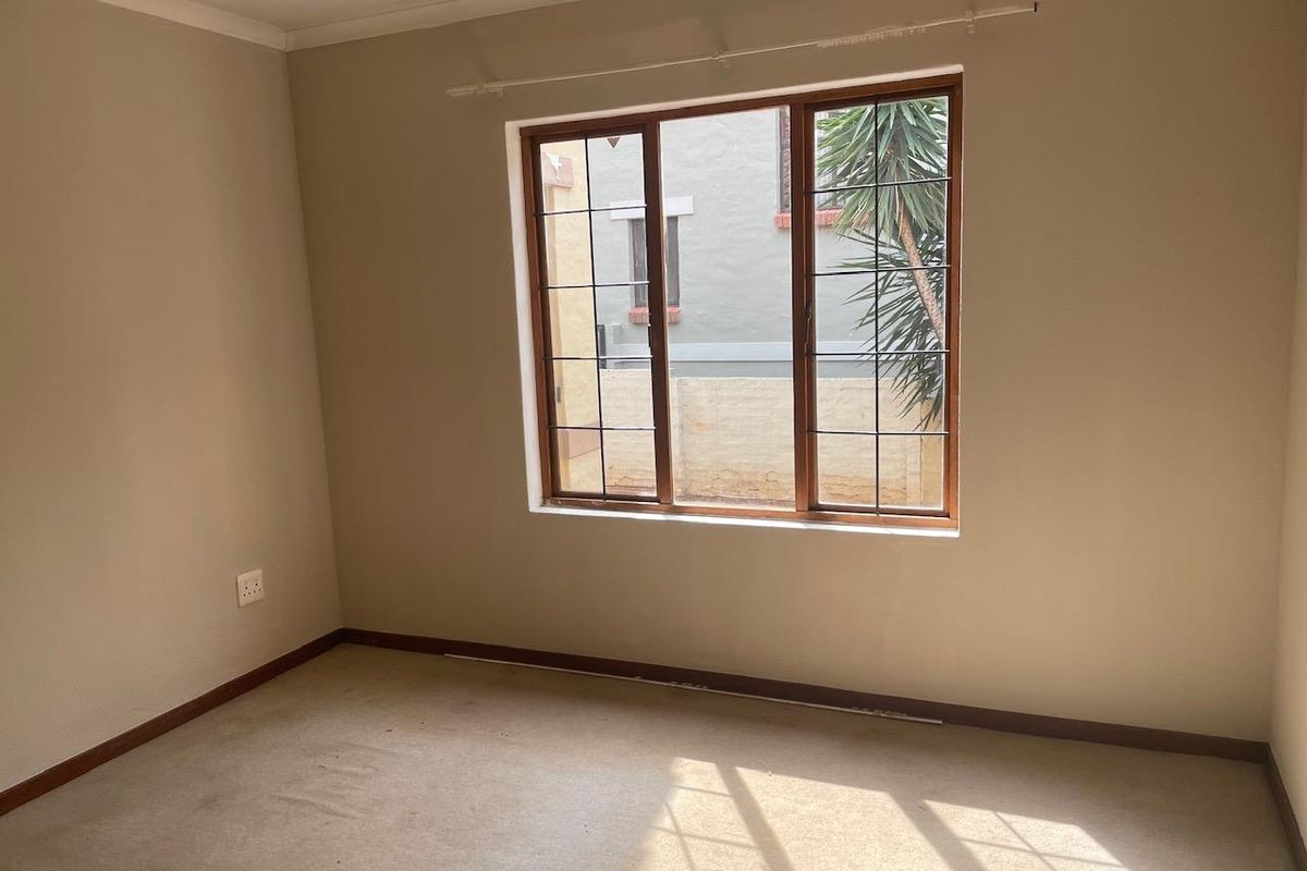 An empty bedroom featuring neutral wall tones, carpeted flooring, and a large timber-framed window allowing natural light.
