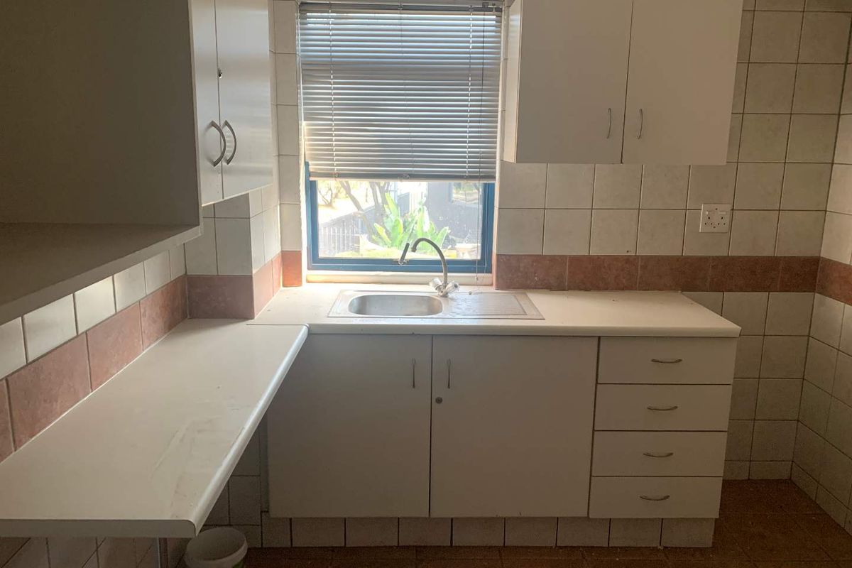 A functional office kitchenette featuring built-in white cabinetry, a stainless steel sink, and tiled wall finishes with a window providing natural light.