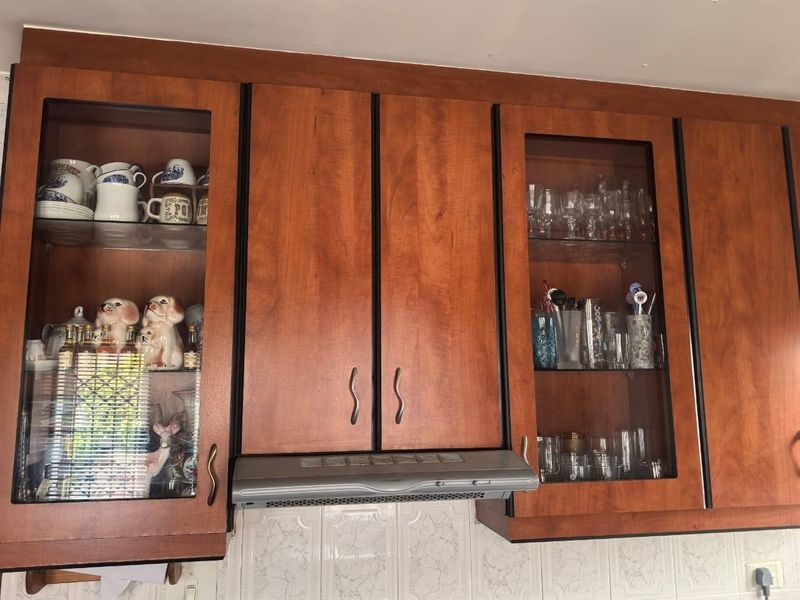A kitchen view featuring wooden cabinetry with glass-fronted display sections, an integrated extractor fan, and a tiled backsplash.