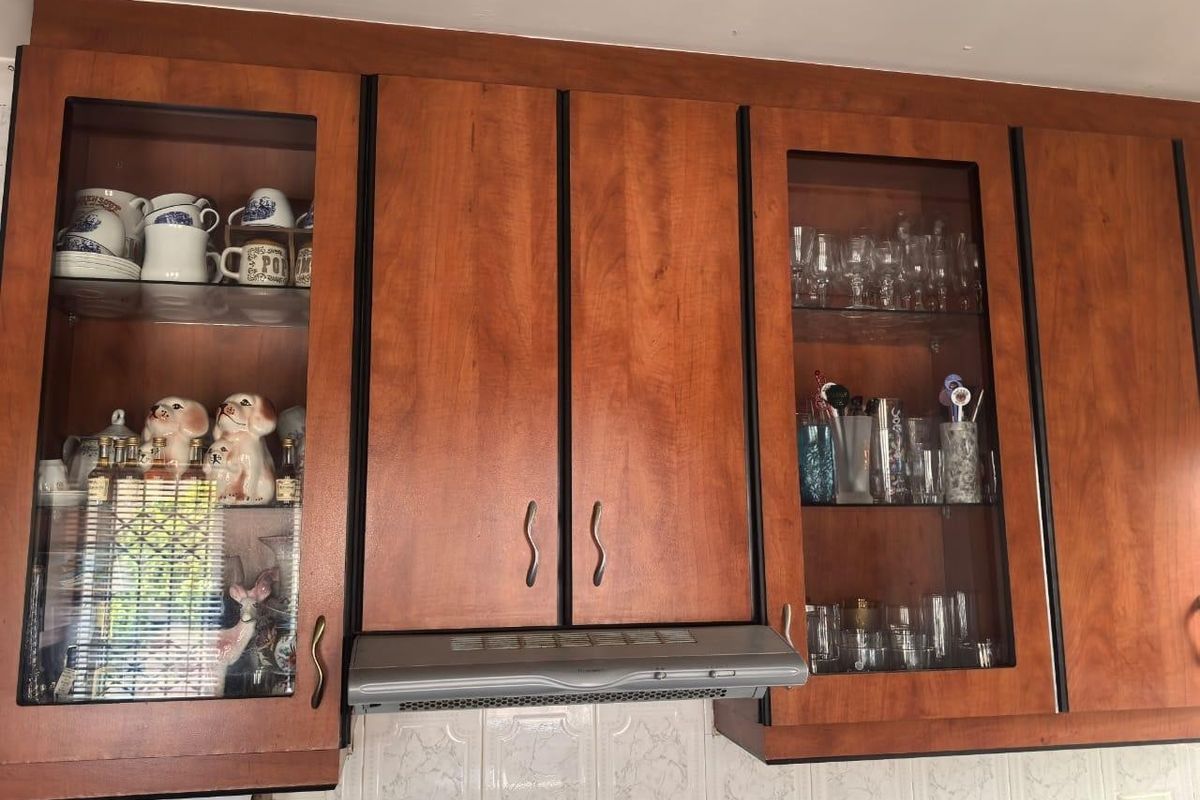 A kitchen view featuring wooden cabinetry with glass-fronted display sections, an integrated extractor fan, and a tiled backsplash.